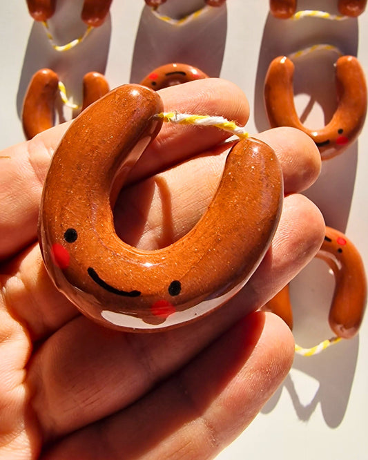 Hand holding a smiling ceramic Alheirita brooch/magnet, shaped like a small horseshoe sausage