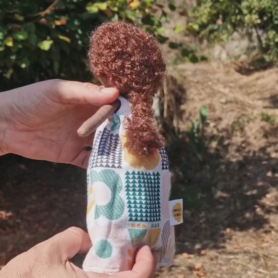 Hands showing how a midsize reversible fabric doll turns inside out, with blonde hair on one side and brown curly hair on the other, by Molli & Moai