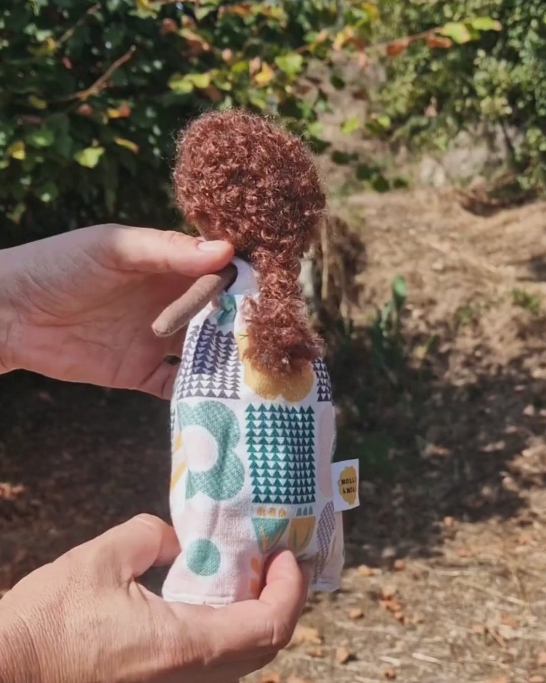 Hands showing how a midsize reversible fabric doll turns inside out, with blonde hair on one side and brown curly hair on the other, by Molli & Moai